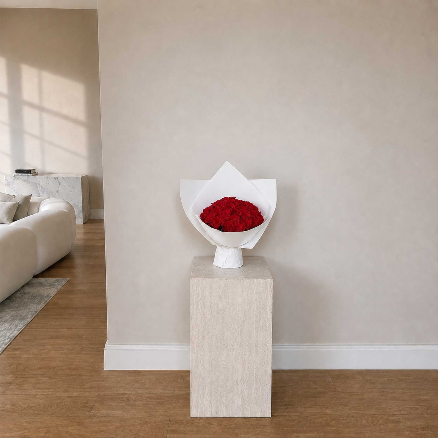 Bouquet of red roses in a white paper wrap on a beige pedestal in a living room.