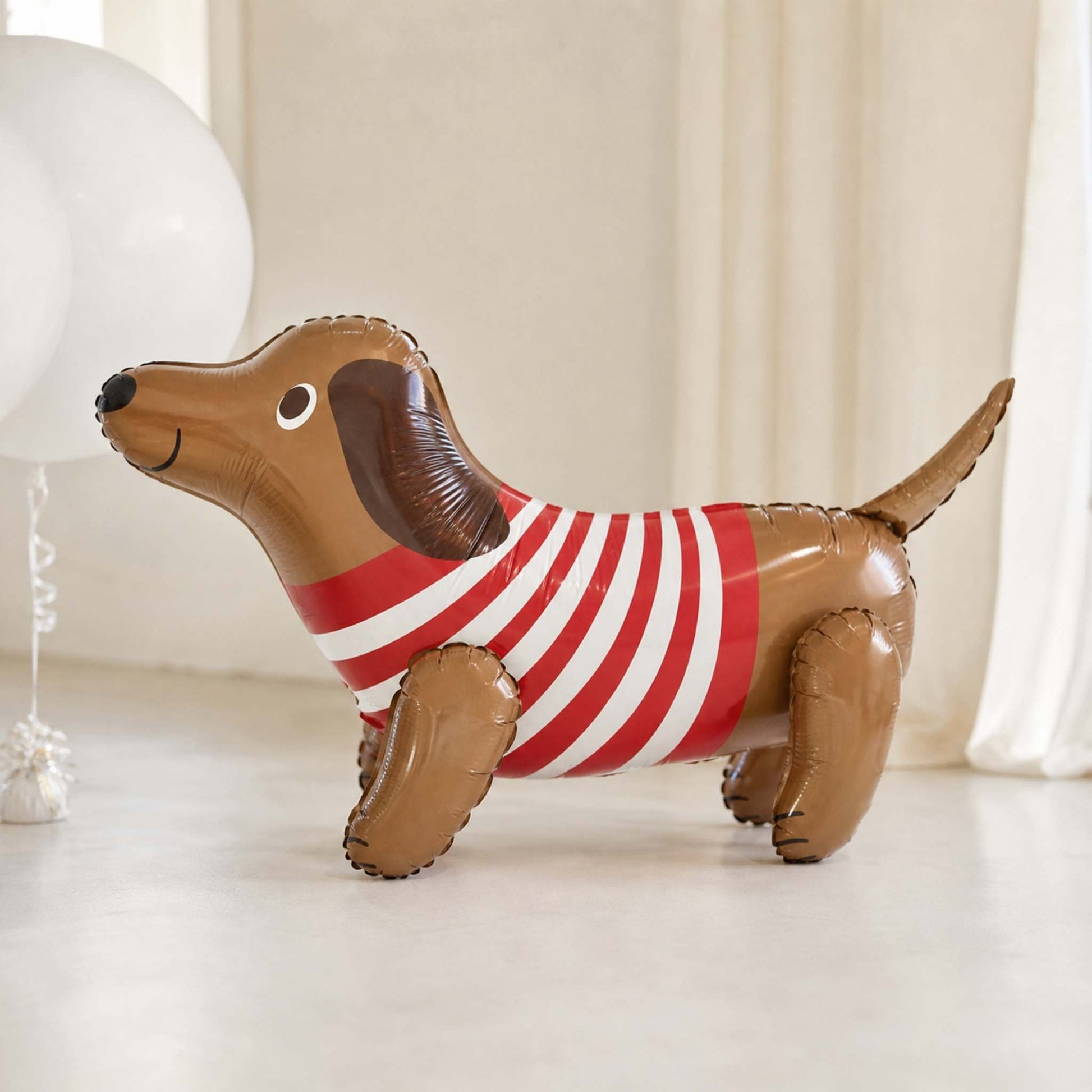 Inflatable dachshund balloon with a red and white striped shirt on a light background