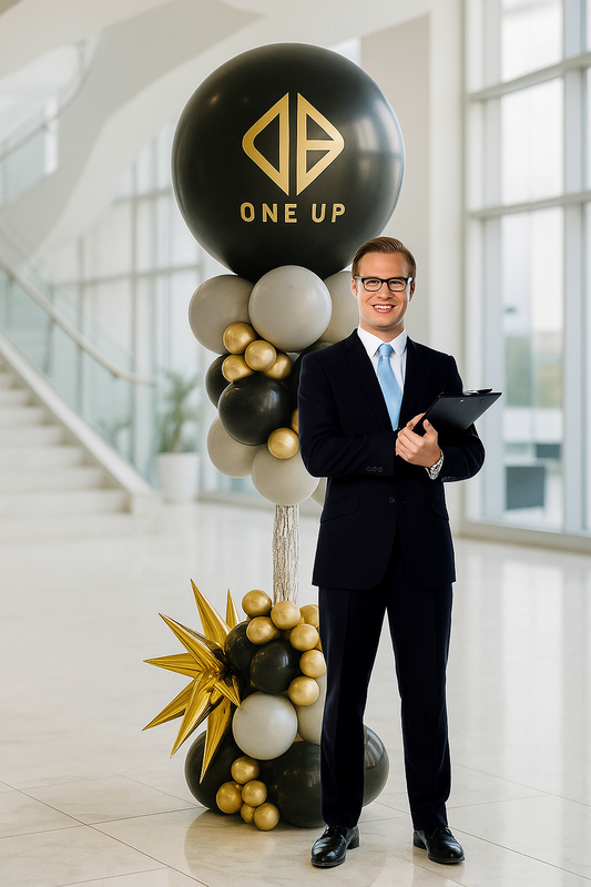 Man in a suit standing next to a balloon arrangement with 'ONE UP' branding in an indoor setting.