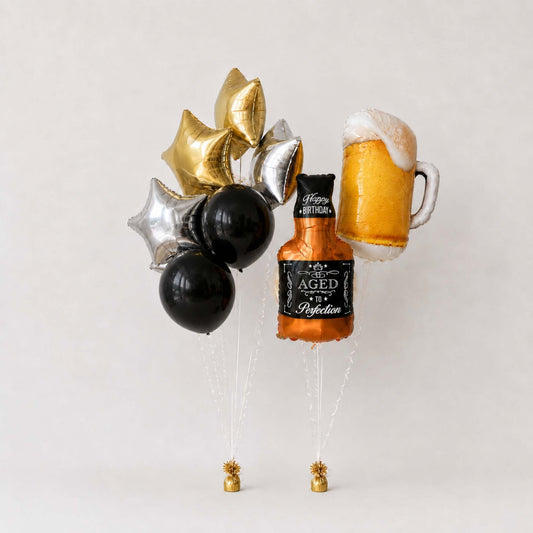 A birthday party decoration set featuring a metallic foil bottle balloon labeled 'Aged 45 Celebration' and 'Happy Birthday', a metallic beer mug balloon, and a cluster of black, silver, and gold balloons on clear stands against a light gray background.