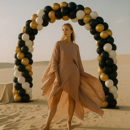 Woman in a flowing dress standing in front of a balloon arch in a desert setting