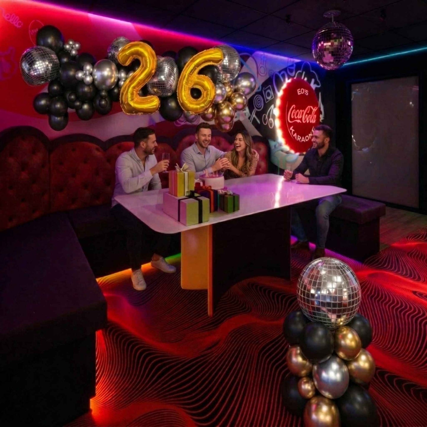 People celebrating a 26th birthday with decorations and Coca-Cola branding in a themed room.