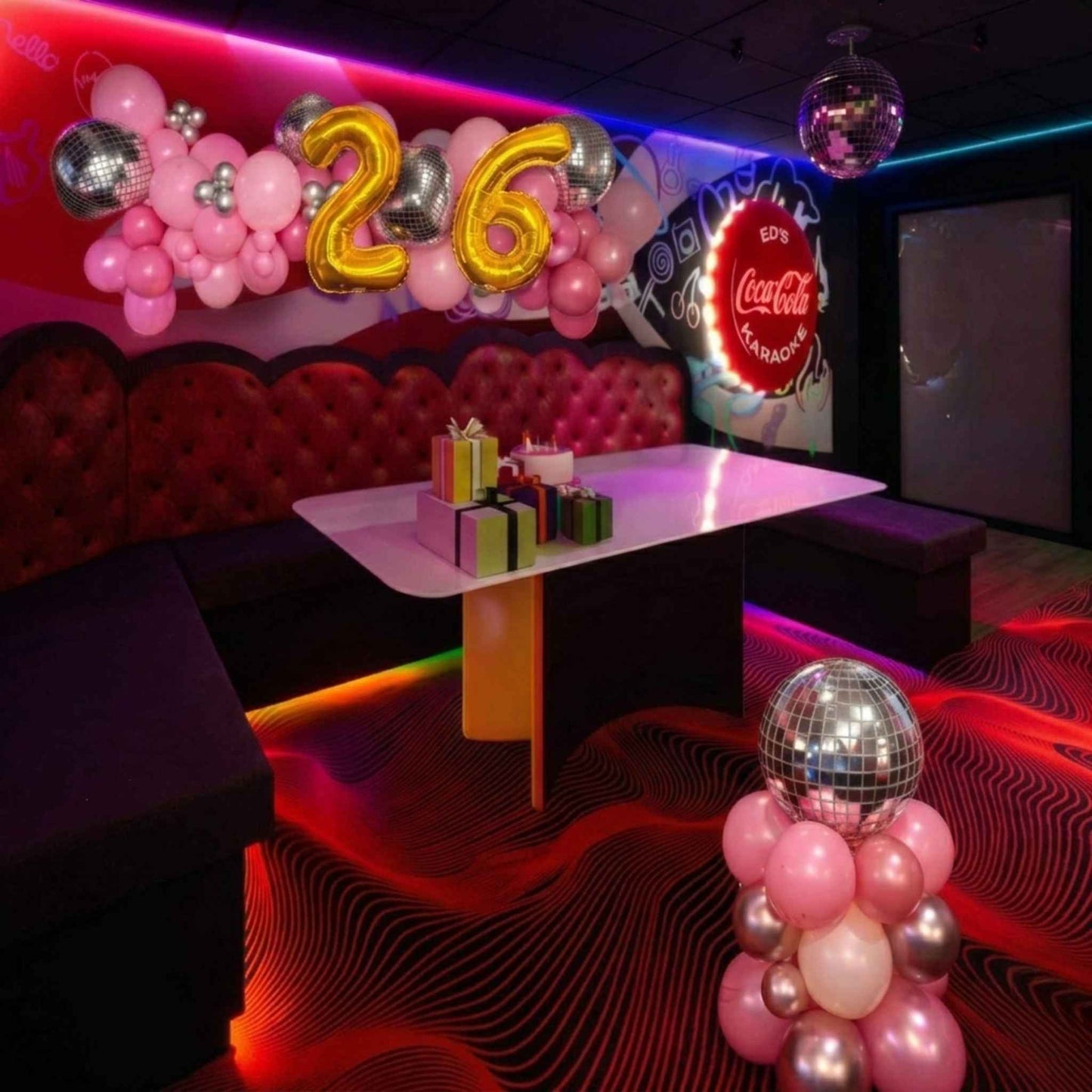 Decorated room with balloons, a cake, and a Coca-Cola sign in a karaoke setting.
