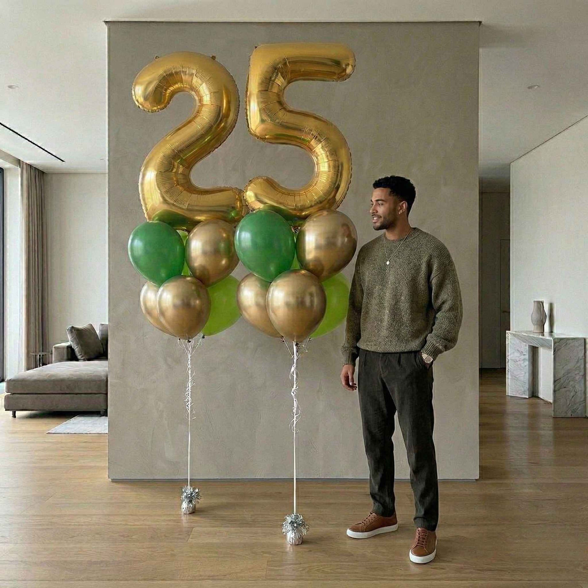 Man standing next to a large '25' balloon arrangement in a modern living room.