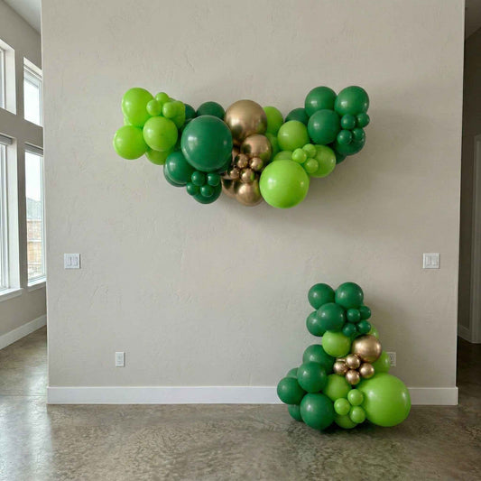 Green and gold balloon garland decorations on a plain wall