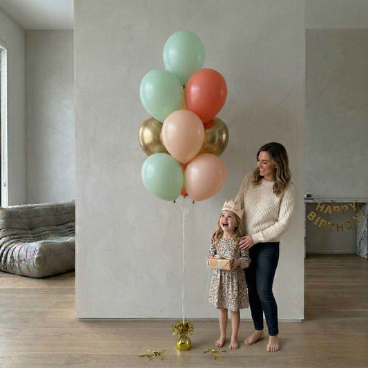Woman and child with colorful balloons in a room with 'Happy Birthday' banner.