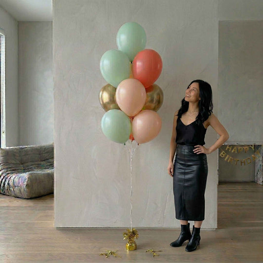 Woman standing next to a large bouquet of colorful balloons in a room with a 'Happy Birthday' banner.