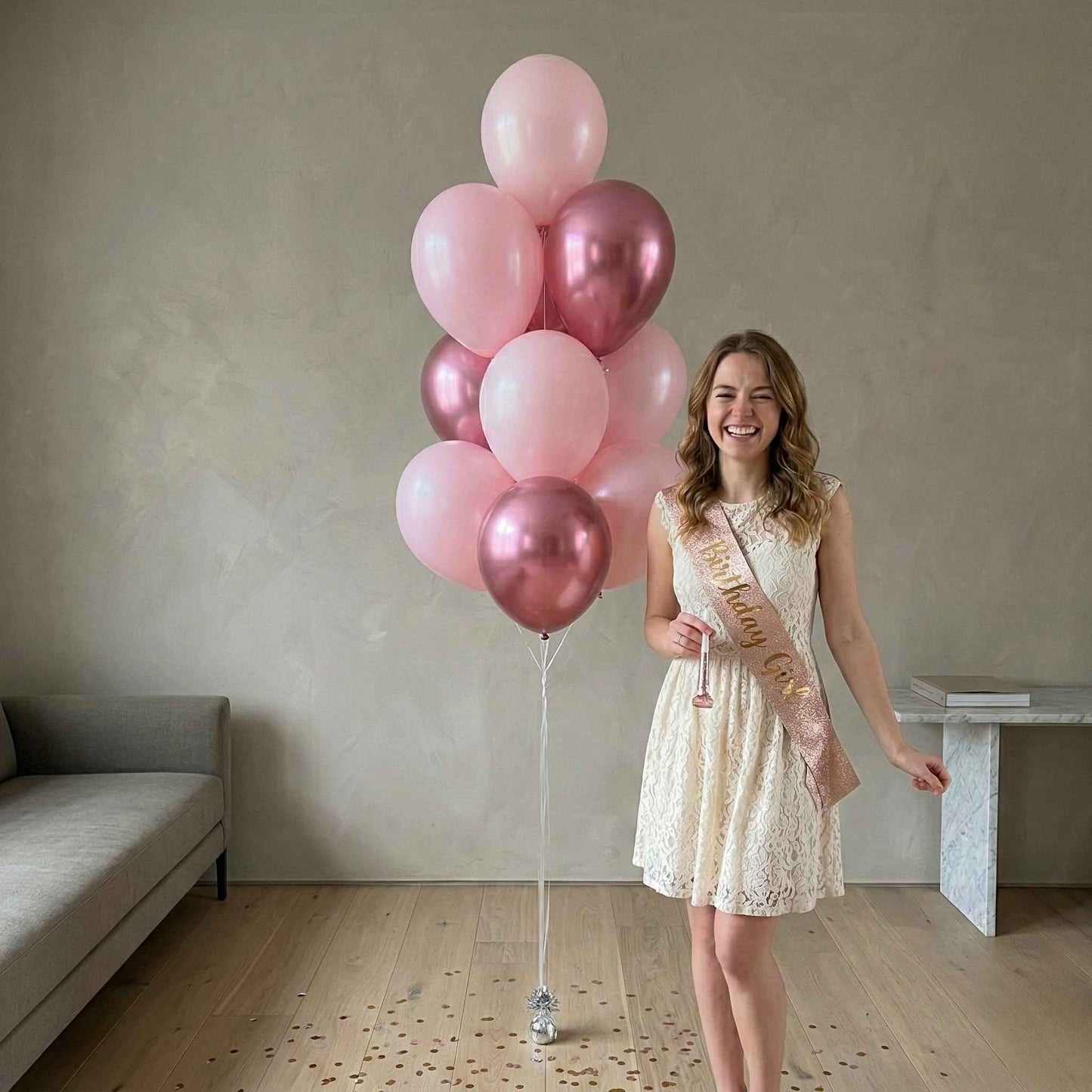 Woman holding pink and gold balloons in a room with a couch and table.