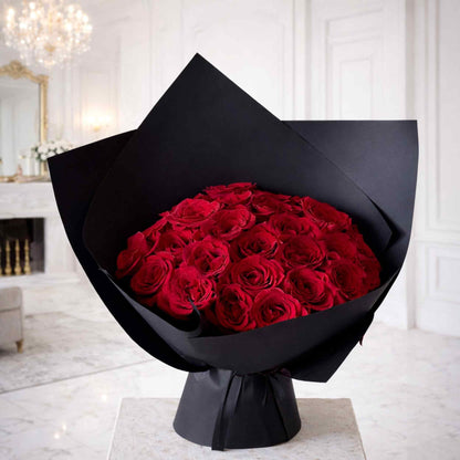 Bouquet of red roses wrapped in black paper on a white surface with a decorative background.