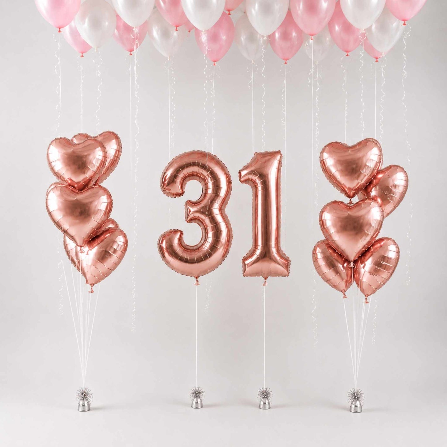 Rose gold foil balloons arranged as two heart-shaped balloon clusters on each side of metallic number 31 balloons, with pink and white balloons floating at the top against a light gray background.