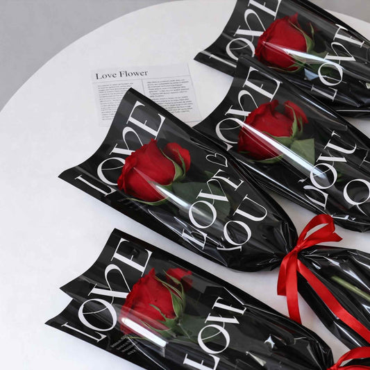 Red roses in black packaging with 'LOVE' text on a white surface