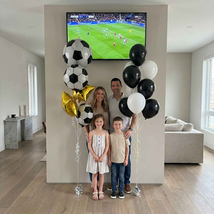 Family with soccer-themed balloons in a living room watching a soccer match on TV.
