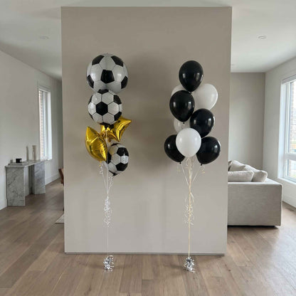 Two sets of balloons, one with soccer ball designs and the other with black, white, and gold balloons, against a neutral wall.