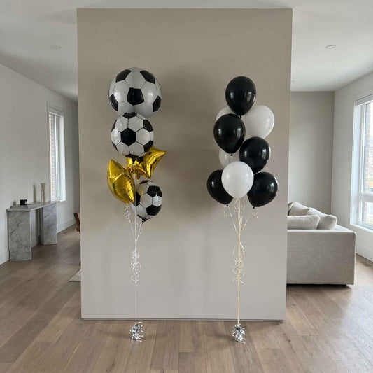 Two sets of balloons, one with soccer ball designs and the other with black, white, and gold balloons, against a neutral wall.