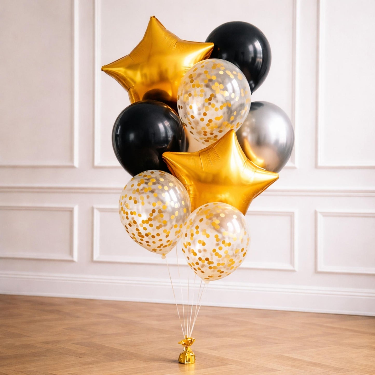 Bouquet of gold, black, and silver balloons against a white wall.