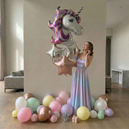 Woman in a pastel dress holding a unicorn-shaped balloon surrounded by colorful balloons in a room.