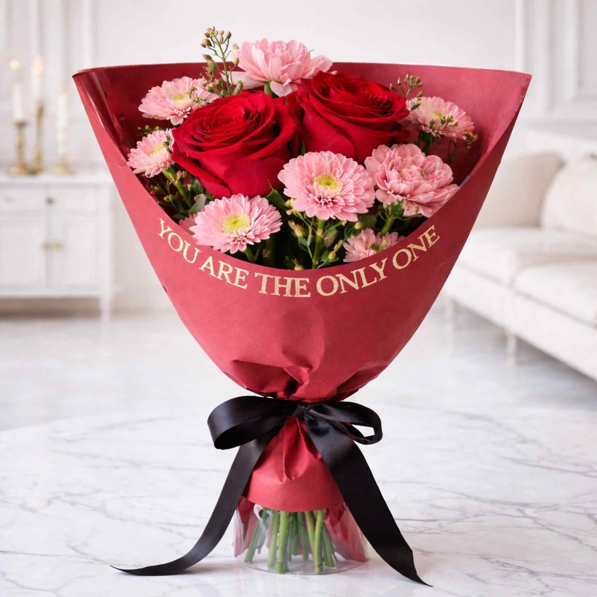 Bouquet of red and pink flowers wrapped in red paper with 'YOU ARE THE ONLY ONE' text, placed on a light-colored floor.