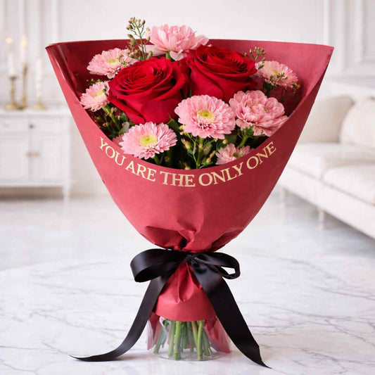 Bouquet of red and pink flowers wrapped in red paper with 'YOU ARE THE ONLY ONE' text, placed on a light-colored floor.