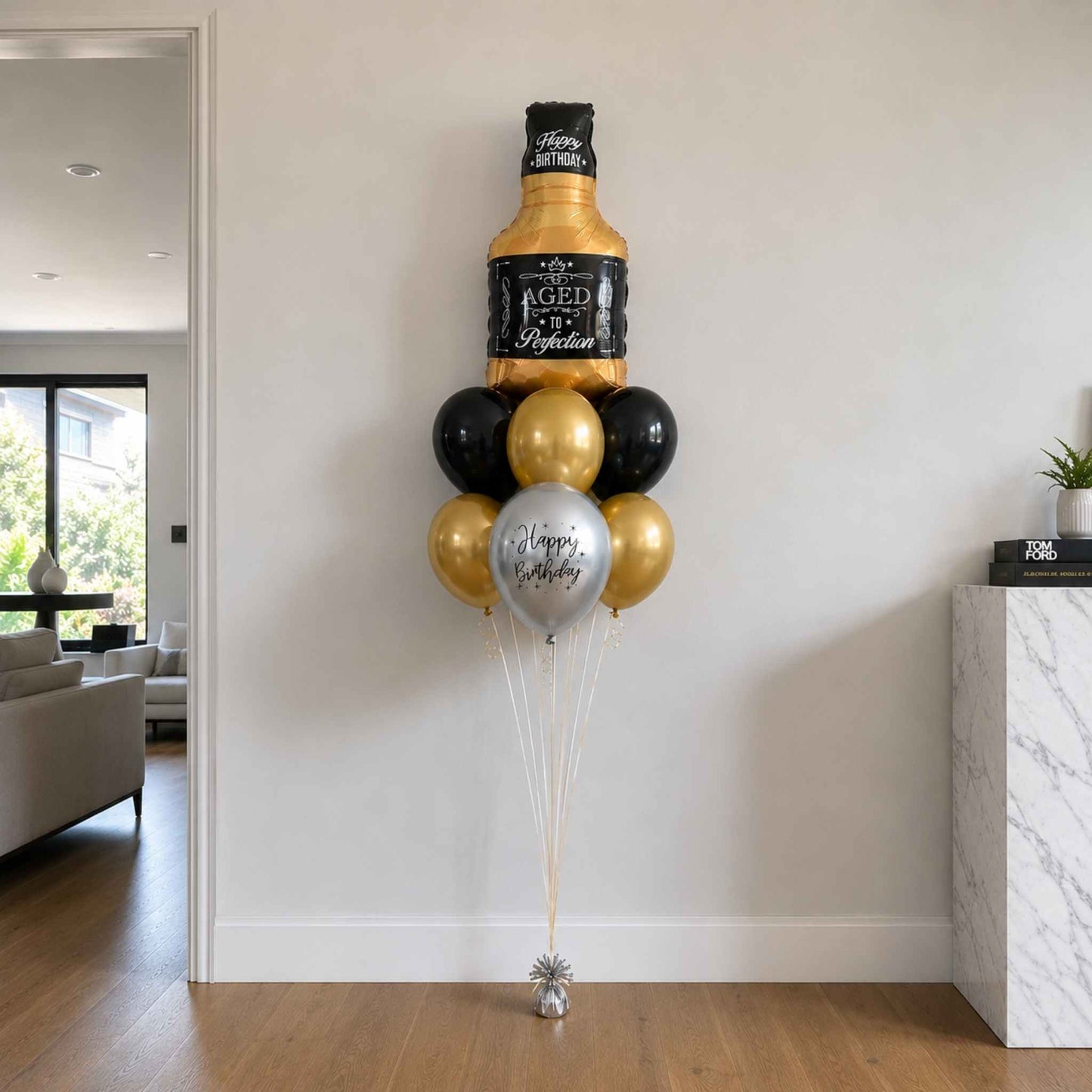 Aged to Perfection whisky bottle foil balloon bouquet with black, chrome gold, and silver helium balloons styled in a modern luxury home setting.