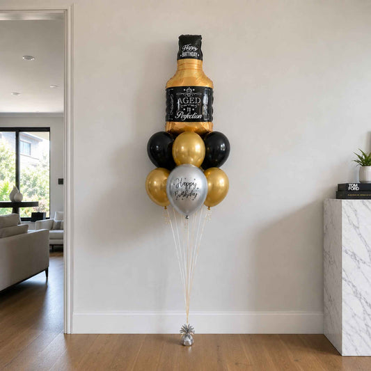 Aged to Perfection whisky bottle foil balloon bouquet with black, chrome gold, and silver helium balloons styled in a modern luxury home setting.
