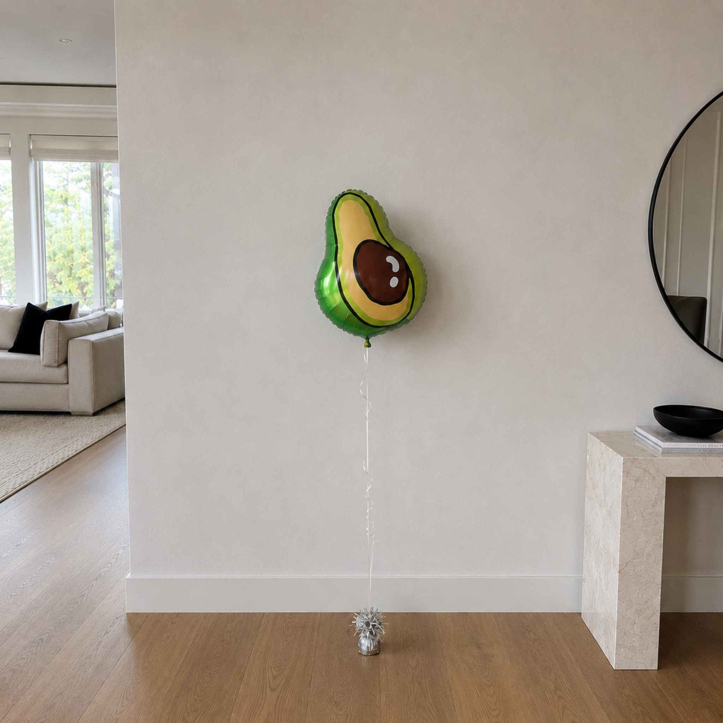 Avocado-shaped balloon on a string in a room with a couch and mirror.