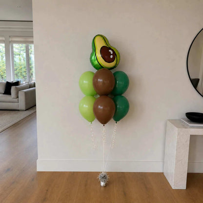 Avocado-shaped balloon and green, brown, and red balloons against a wall in a living room.