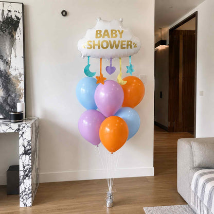 Baby shower balloon bouquet with white Baby Shower cloud foil balloon, pastel blue, purple, and orange helium balloons, and hanging moon, star, and heart accents on silver weight in a modern home.