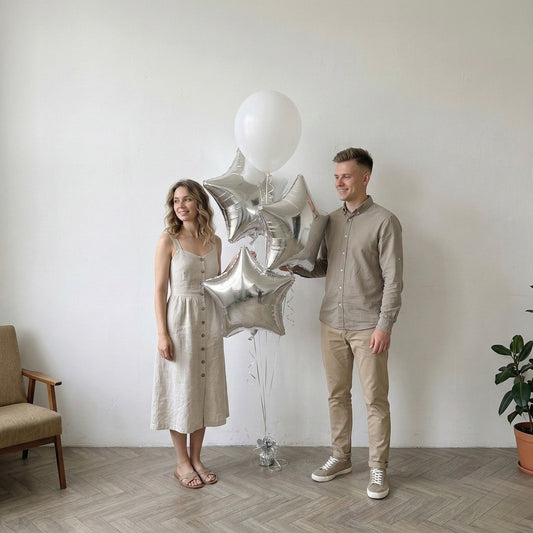Man and woman standing with silver star foil balloon bouquet in a room with a chair and plant.