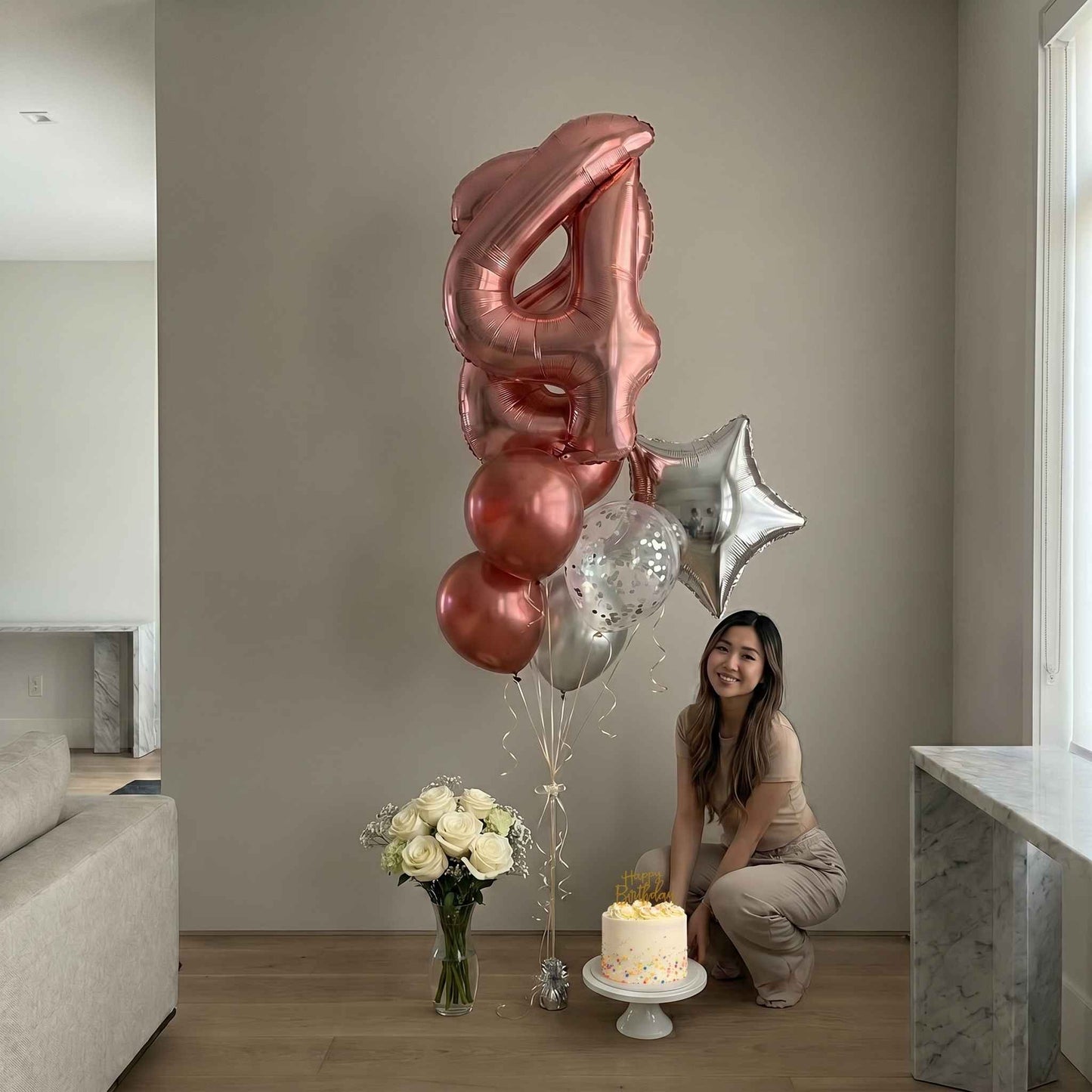 Woman with birthday cake and balloons in a room.