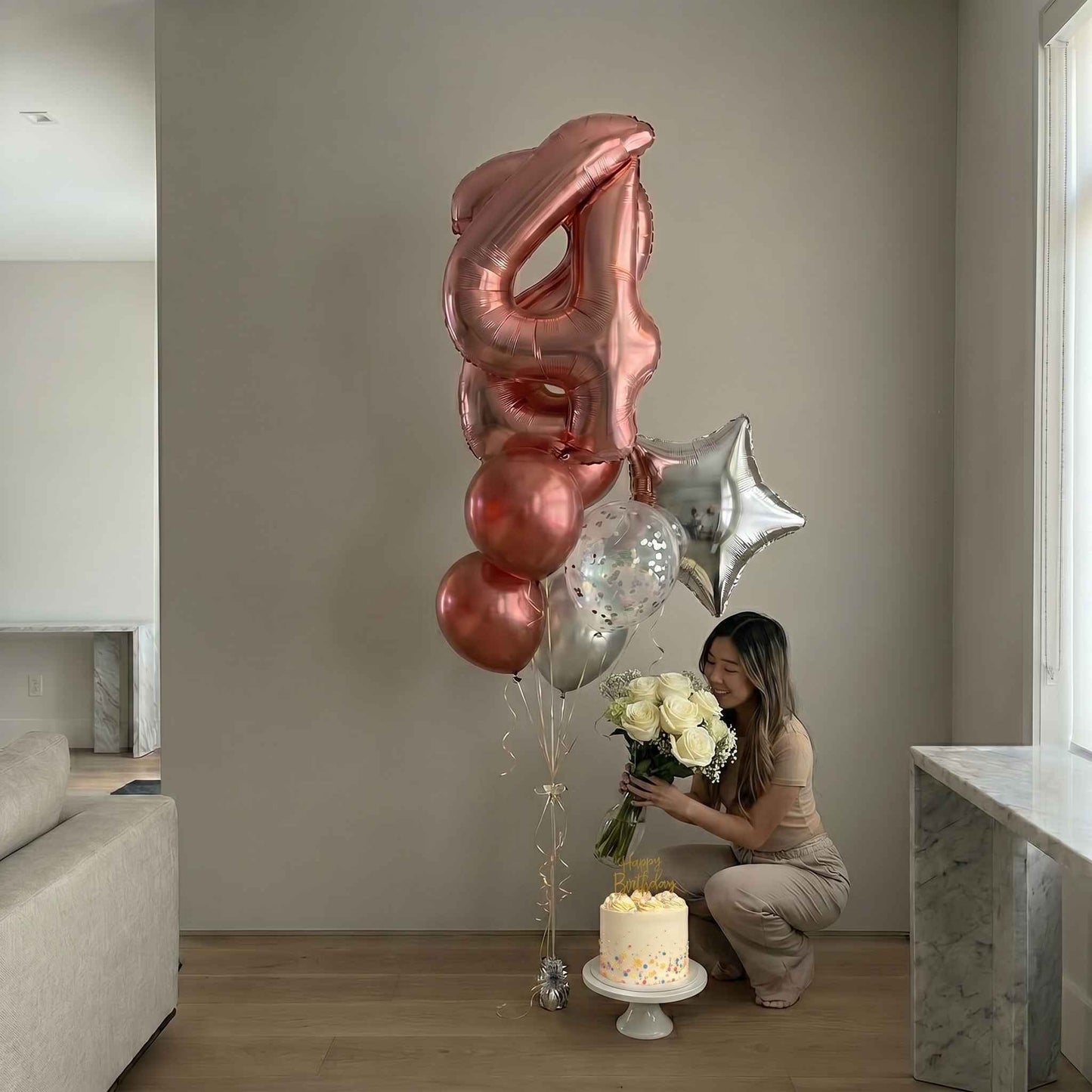 Woman with balloons and flowers in a room with a cake on a stand.
