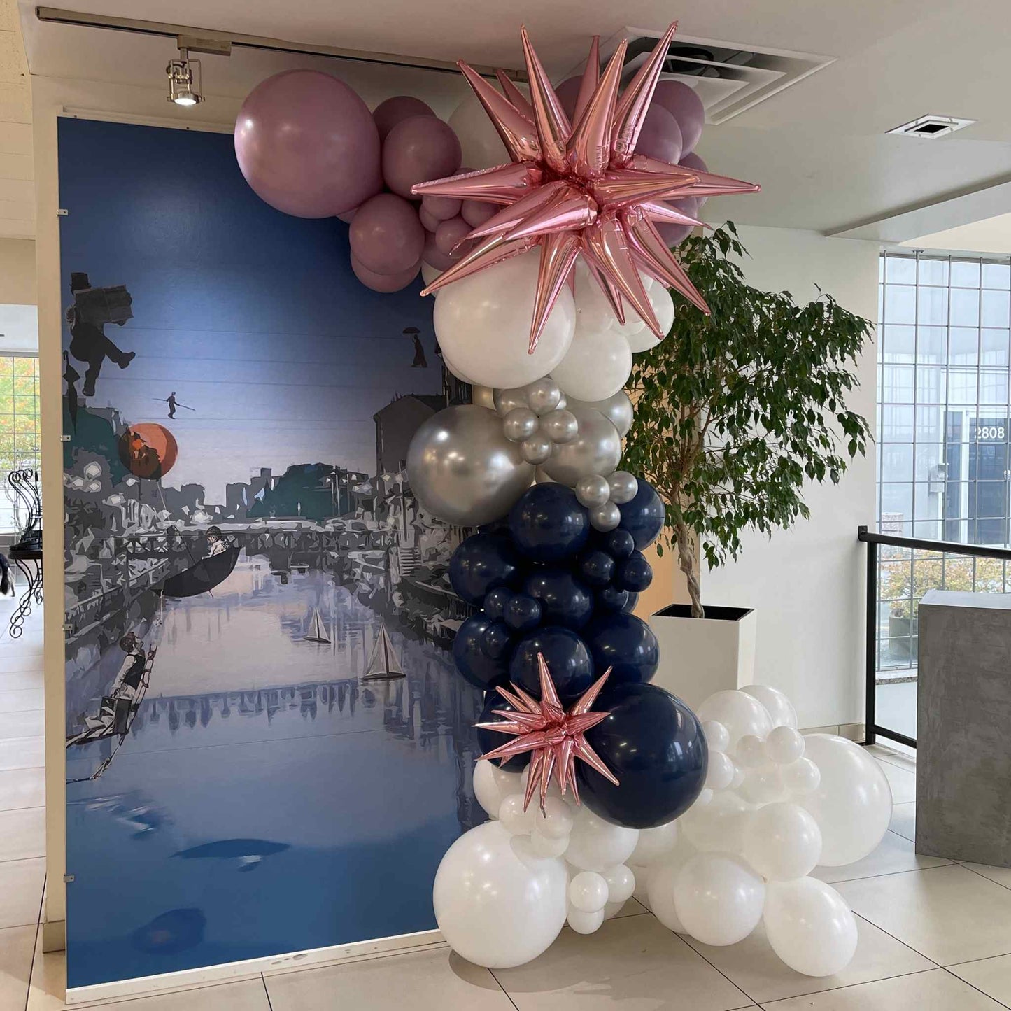 Balloon arch with pink and blue balloons in front of a scenic backdrop