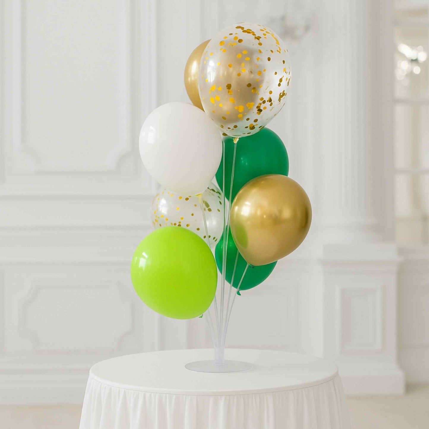 Decorative balloon arrangement with gold, green, and white balloons on a white pedestal against a white curtain background.