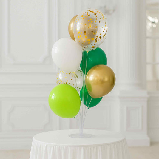 Decorative balloon arrangement with gold, green, and white balloons on a white pedestal against a white curtain background.