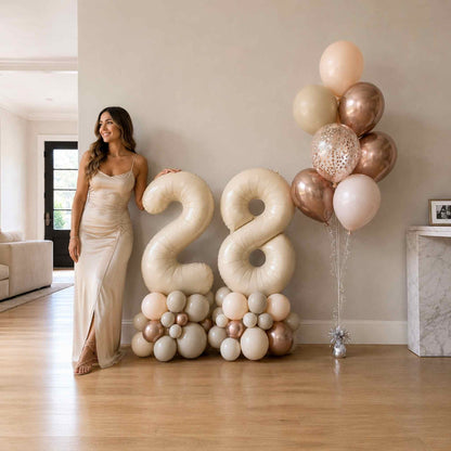 Woman standing next to a large balloon arrangement with the number '28' in a living room.