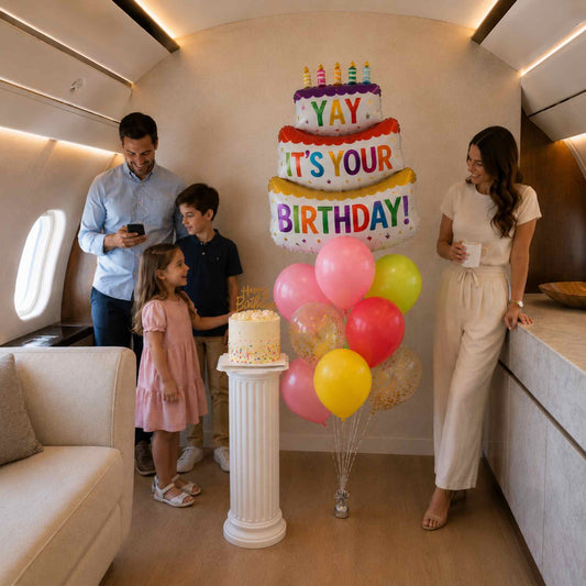 Family celebrating a birthday in a luxurious airplane cabin with balloons and cake.