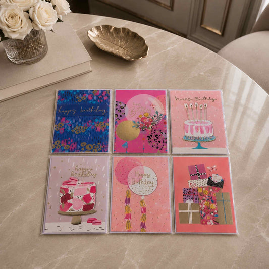 Set of six colorful birthday cards on a marble surface with flowers and a bowl in the background.