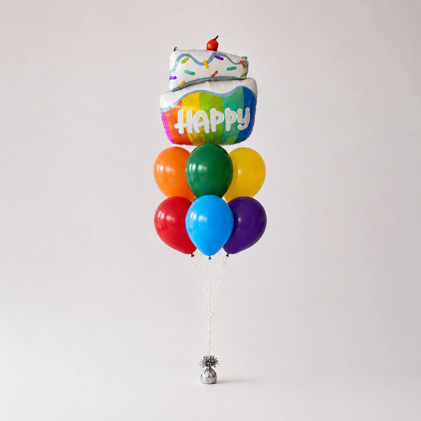 A novelty balloon bouquet shaped like a cupcake with rainbow frosting and a cherry on top, surrounded by eight colorful balloons in red, orange, green, yellow, blue, and purple, tied to a silver tinsel ball on a light gray background.