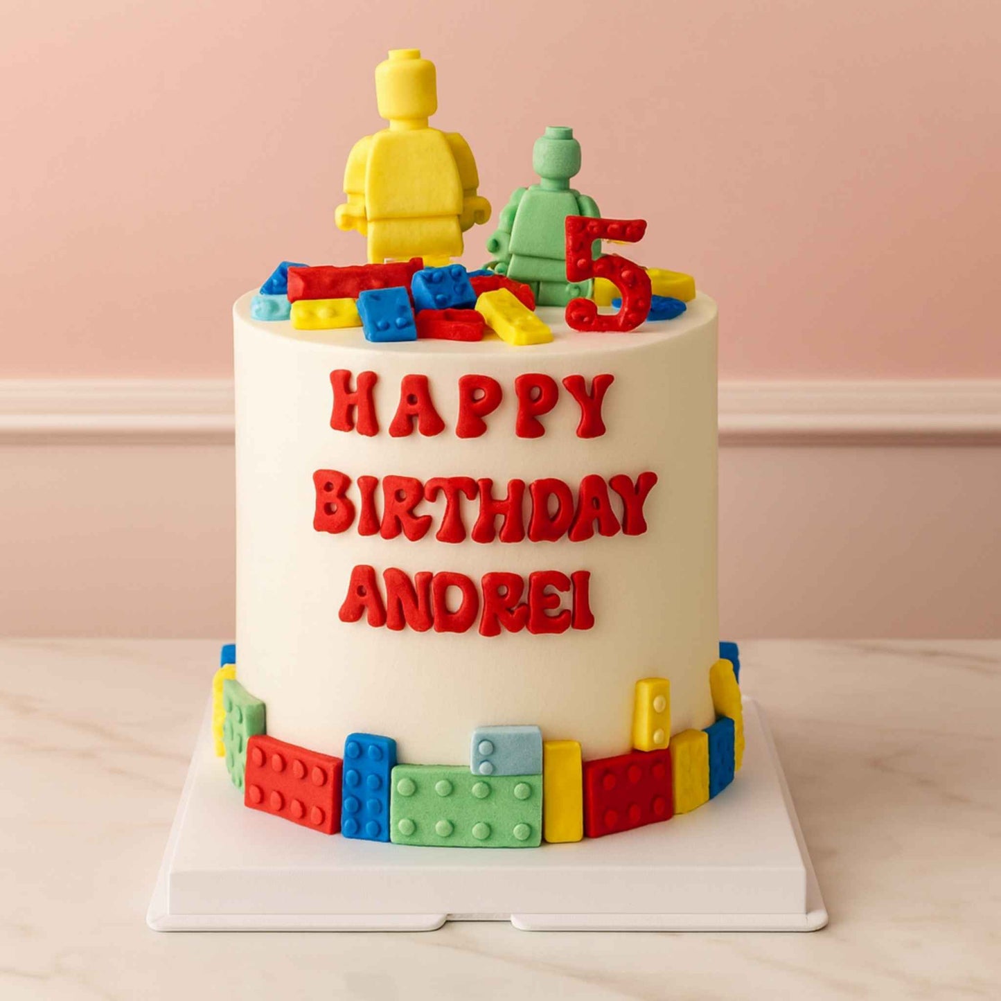 Birthday cake with colorful lego-themed decorations and 'Happy Birthday Andrei!' text on a light pink background.