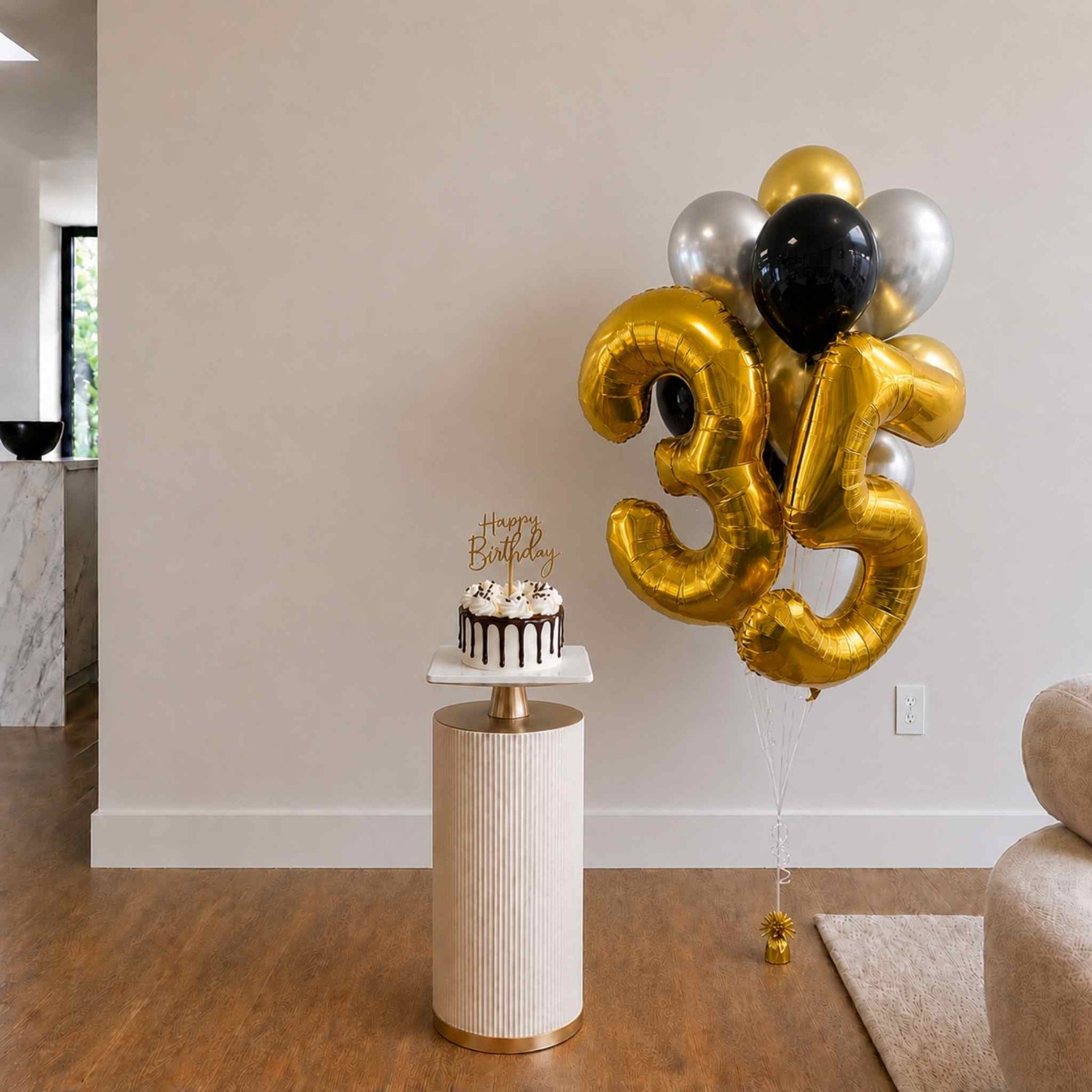 Gold number 35 balloons with a birthday cake on a small table in a room.