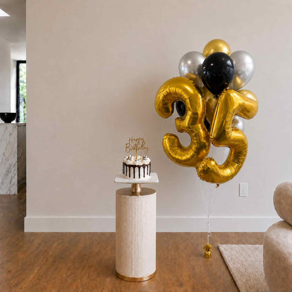 Gold number 35 balloons with a birthday cake on a small table in a room.