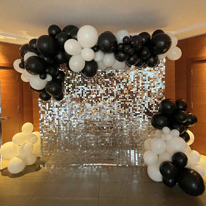 Balloon arch with black and white balloons in front of a glittery sequin curtain.