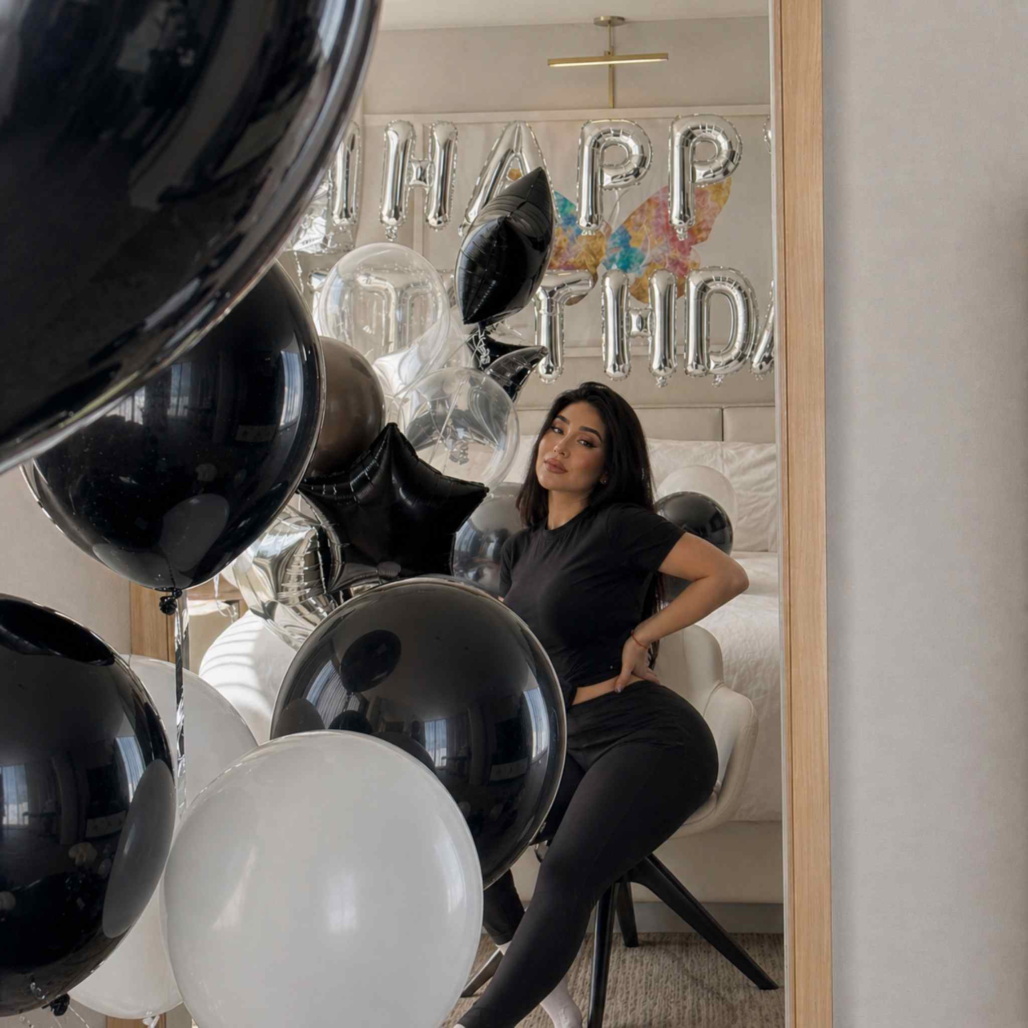 Woman sitting in a room with black and white balloons and 'Happy Birthday' decorations.