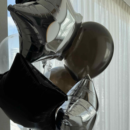 Black and silver balloons against a window with light curtains
