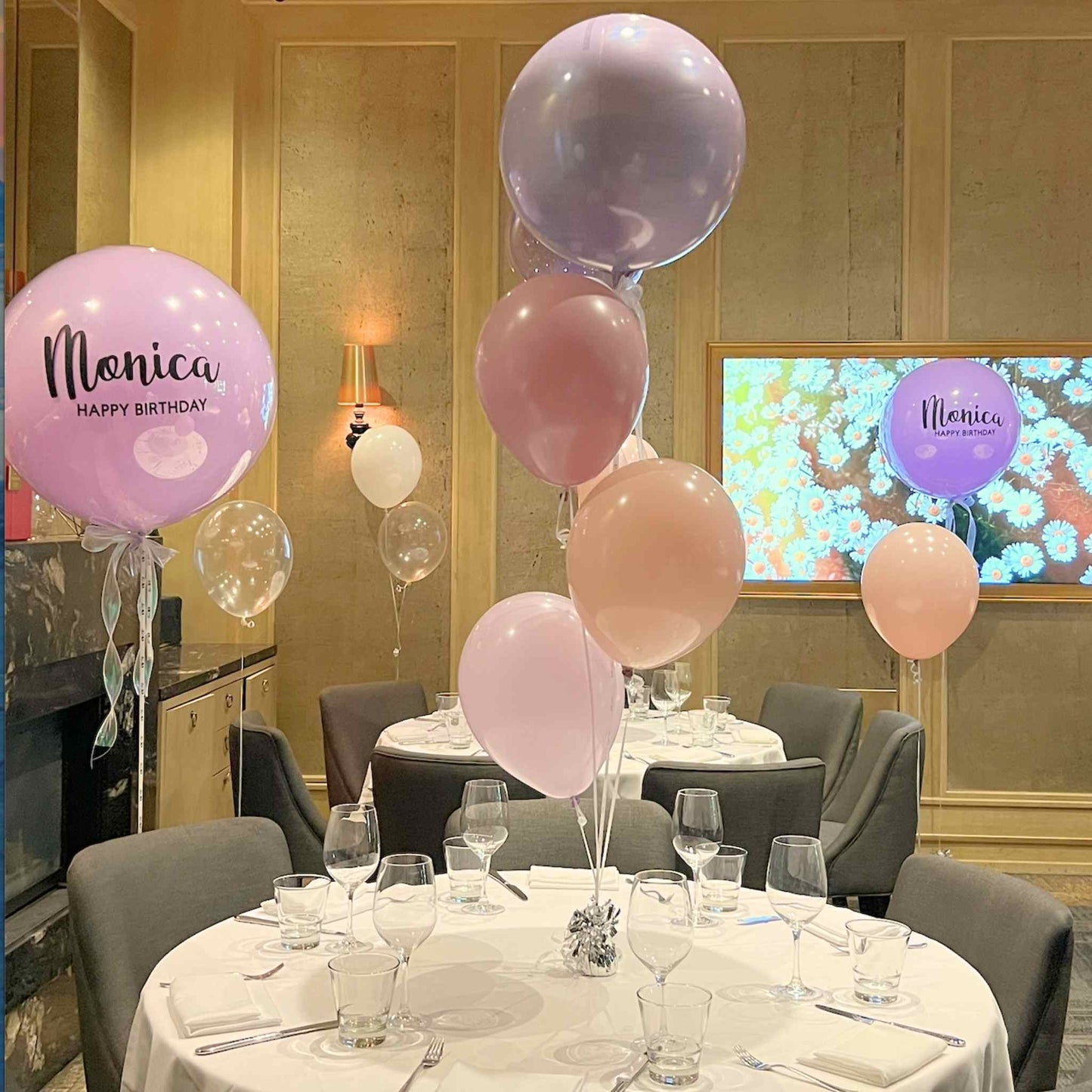 Decorated dining room with balloons and a screen displaying 'Monica Happy Birthday'.
