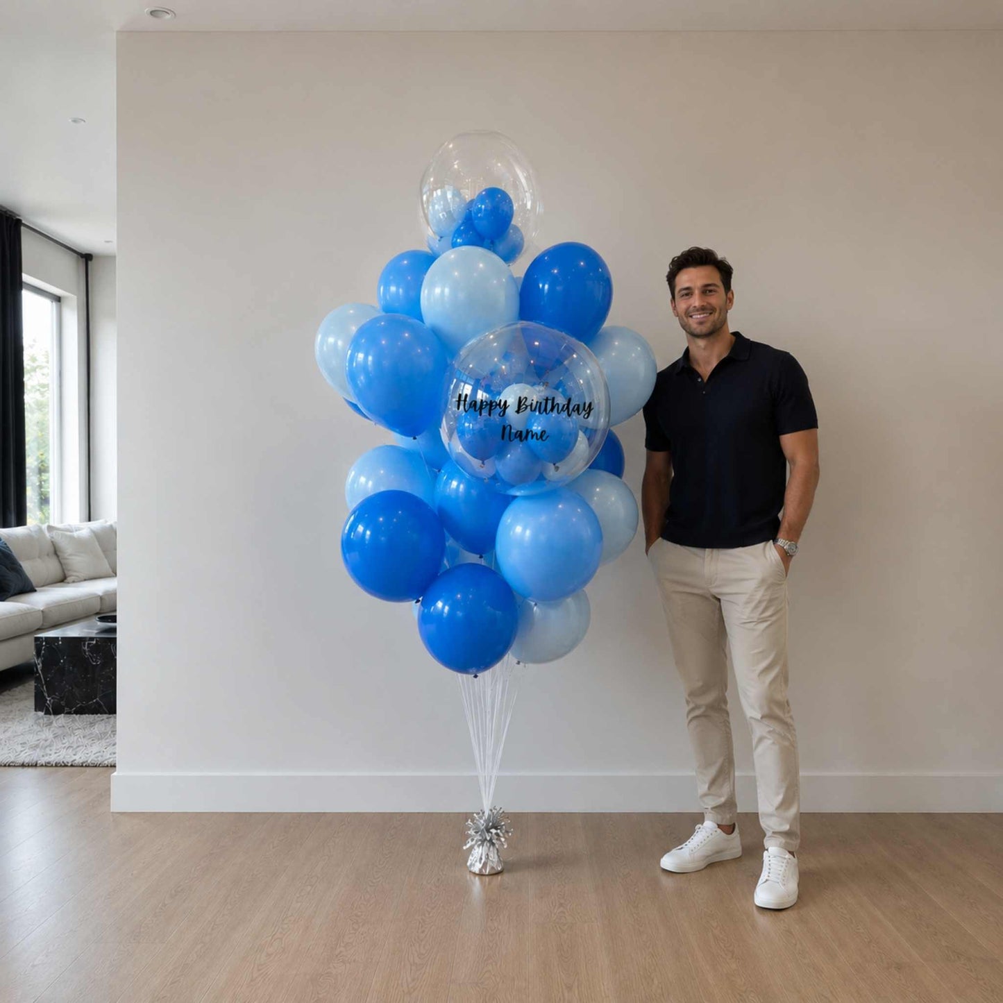 Man standing next to a large bouquet of blue and white balloons indoors.
