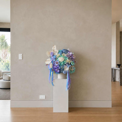 Floral arrangement on a white pedestal against a beige wall