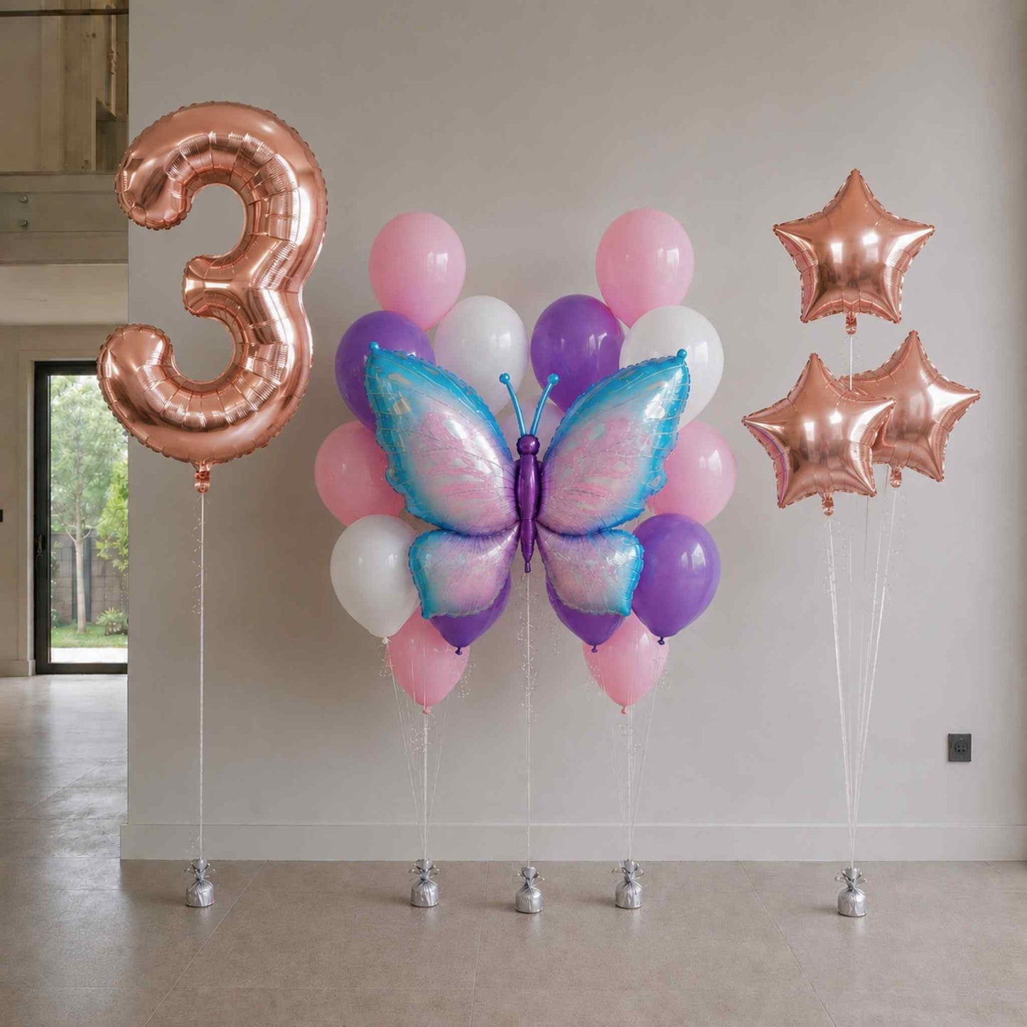 Decorative balloon setup with number '3', butterfly-shaped balloon, and star-shaped balloons against a plain wall.