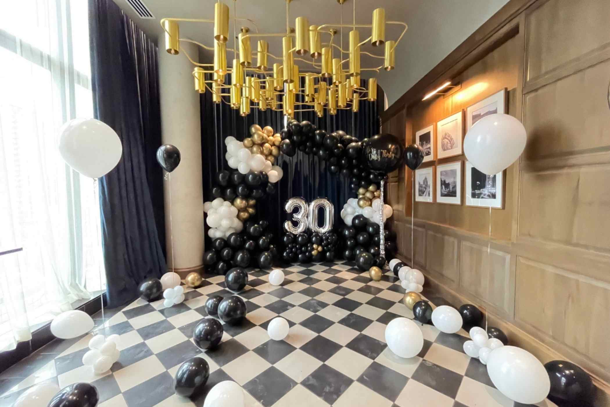 Decorated room with black, white, and gold balloons, a large '30' sign, and a gold chandelier.