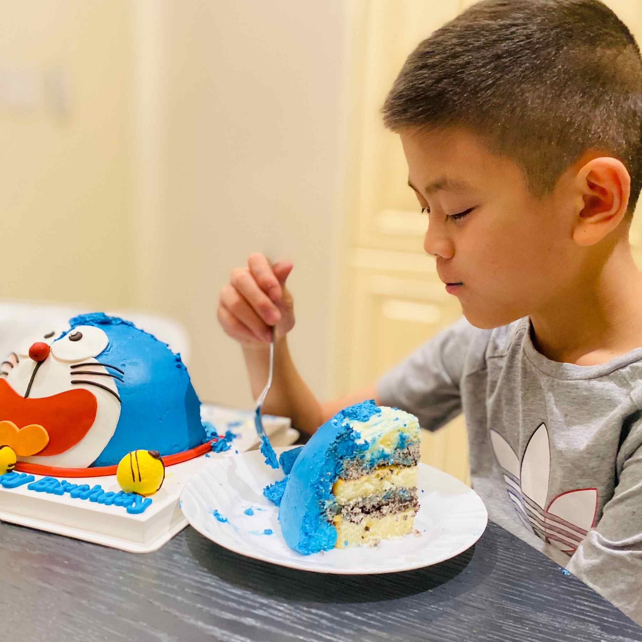 Child eating a slice of blue cake with a cartoon character design on a table.