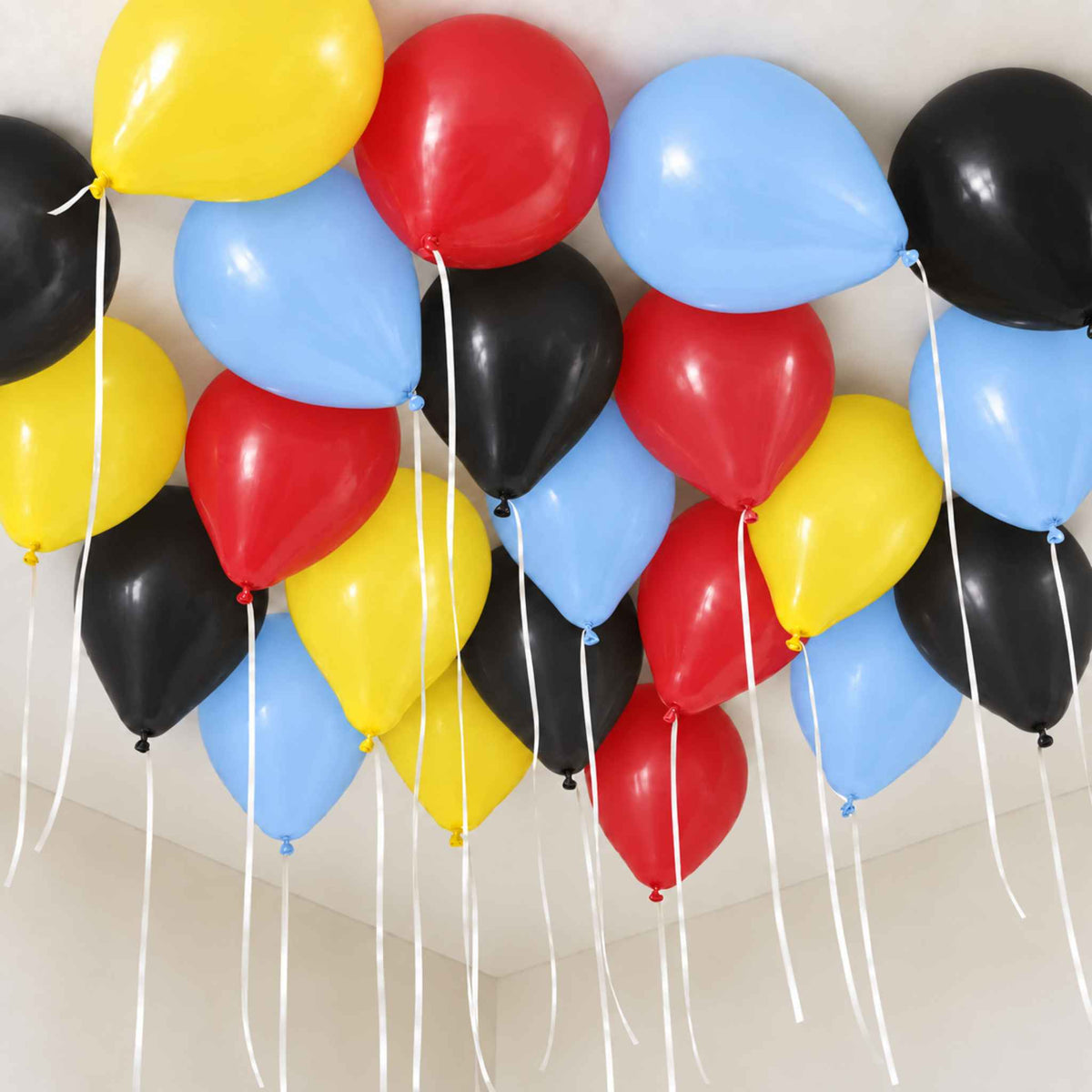 A cluster of latex balloons in black, red, yellow, and light blue, tied to the ceiling of a neutral indoor room.
